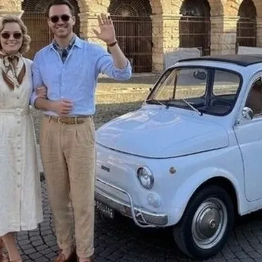 Una coppia in piedi accanto a una Fiat 500 azzurra davanti all'Arena di Verona